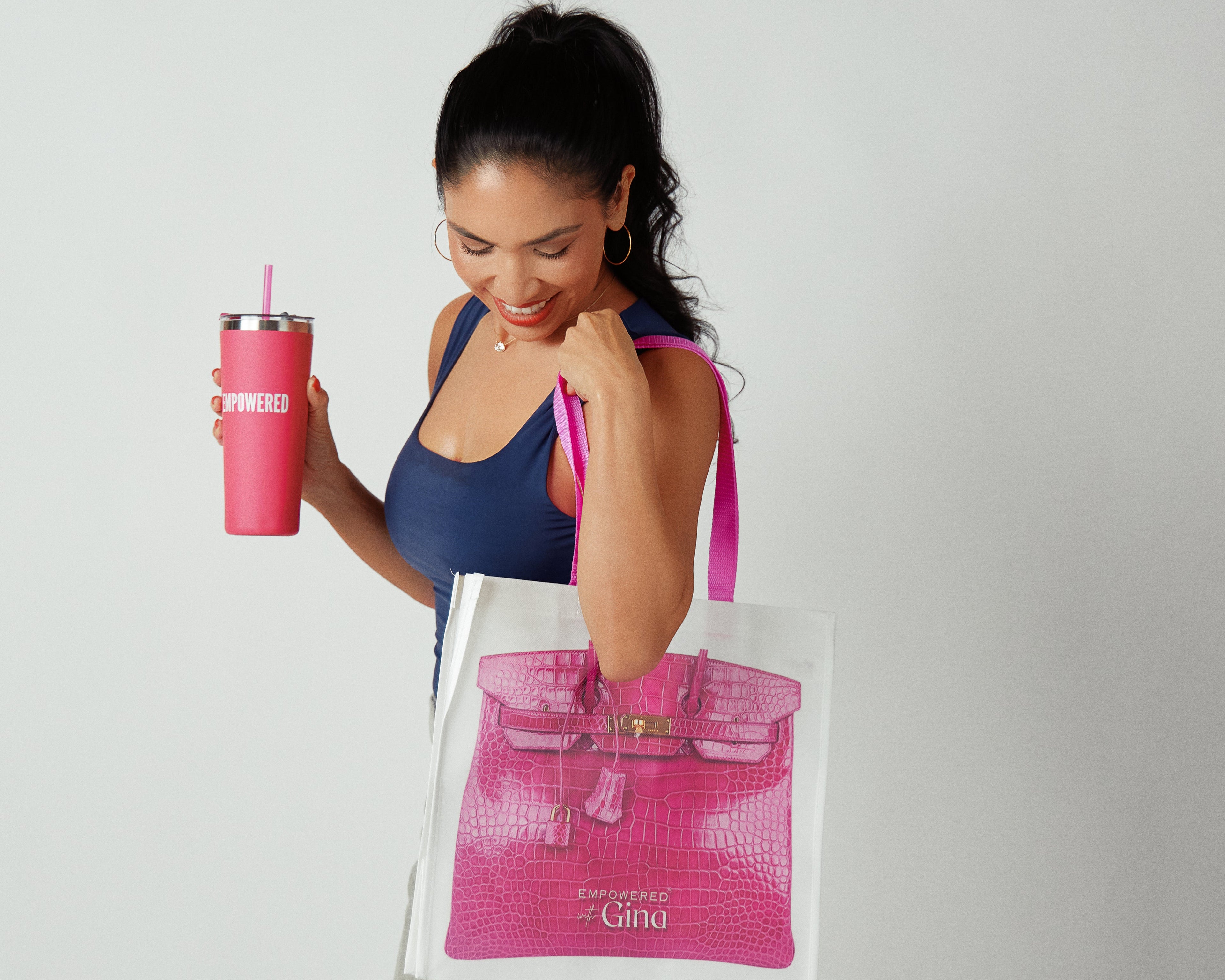 Woman holding a pink tote bag and a pink tumbler with a white background